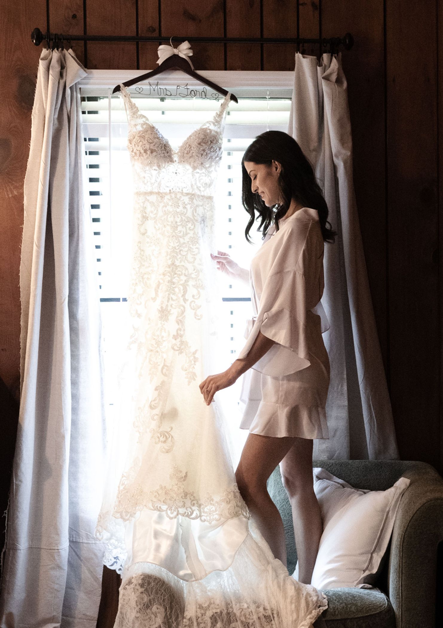 Bride With Her Lace Dress Hanging In Window