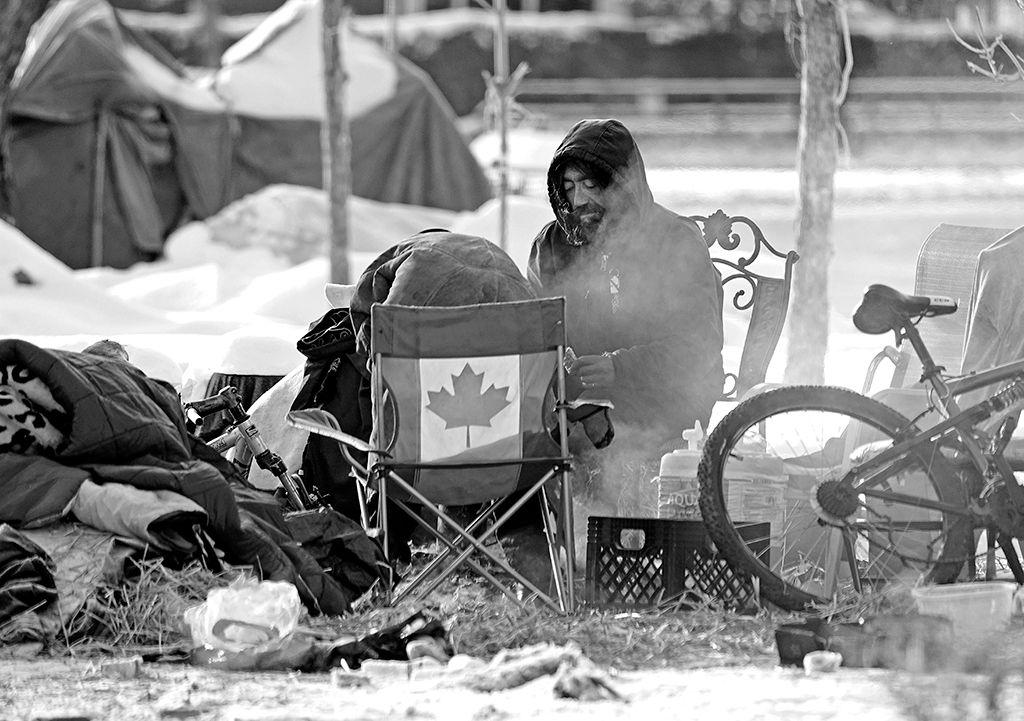 A resident of a homeless camp in Edmonton, Canada tries to keep warm in front of a fire on November 9, 2020.