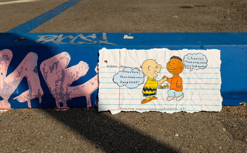 Fine art photograph of a torn algebra notebook page featuring hand-drawn Charlie Brown and Franklin giving dap, with speech bubbles reading "Franklin! That bitch Lucy! Good Grief!" and "Charlie! That smile means Lucy is not around," propped against a blue graffiti-tagged curb on asphalt. From the My Middle School Notebook series by Los Angeles photographer Victor Koroma. Charlie Brown and Franklin Algebra Notes — MY MIDDLE SCHOOL NOTEBOOK | Fine Art Photography | Victor Koroma