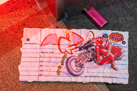 Fine art photograph of a torn notebook page labeled "Anime Club Watch List" featuring a hand-drawn Akira motorcycle scene with "Neo Tokyo" text, listing Cowboy Bebop, Samurai Champloo, Eureka Seven, FLCL, and Dragon Ball Z, with the note "You watch too much Hentai...," photographed on red and grey stone with a pink BIC lighter. From the My Middle School Notebook series by Los Angeles photographer Victor Koroma.
Anime Club Neo Tokyo Watch List — MY MIDDLE SCHOOL NOTEBOOK | Fine Art Photography | Victor Koroma