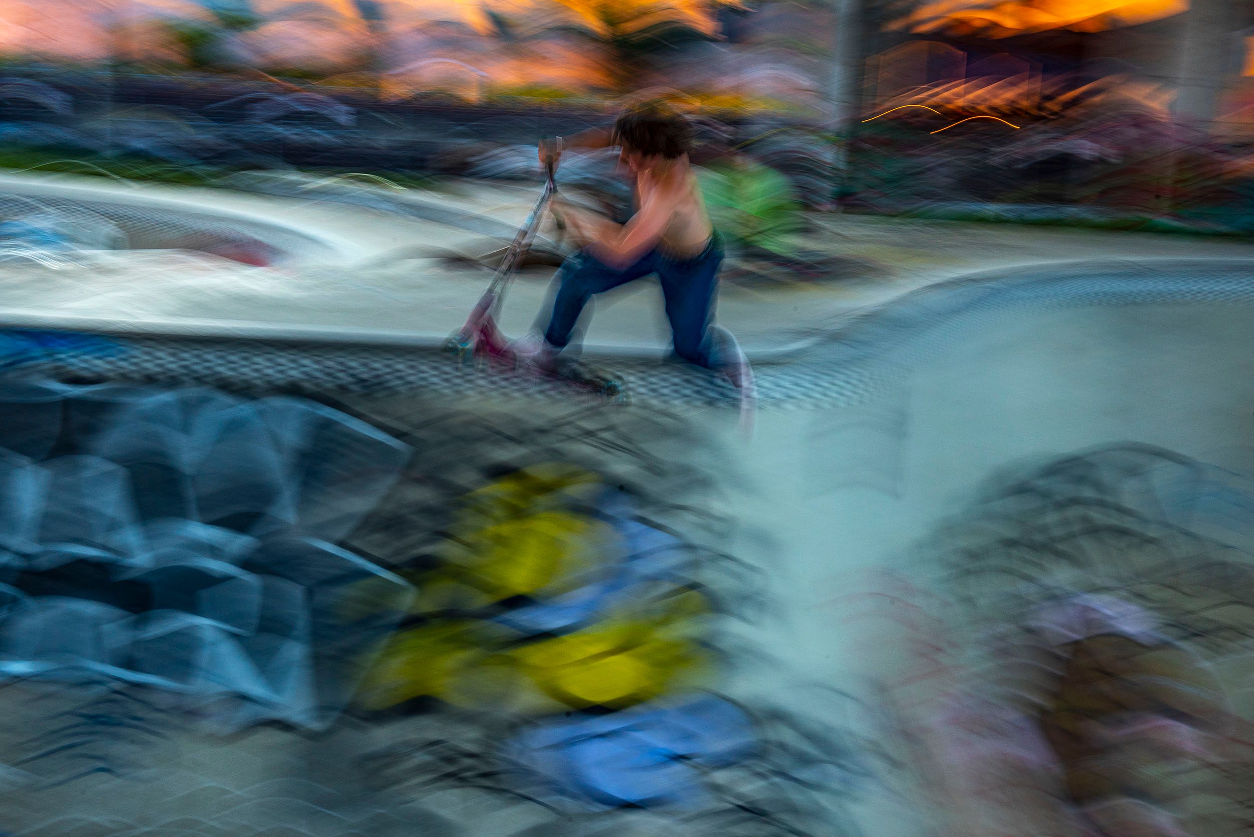 Horizontal color blur motion photograph of scooter rider practicing a run in the cement bowl at dusk at the Lynch Family Skateboard Park, Cambridge, MA Blur Motion