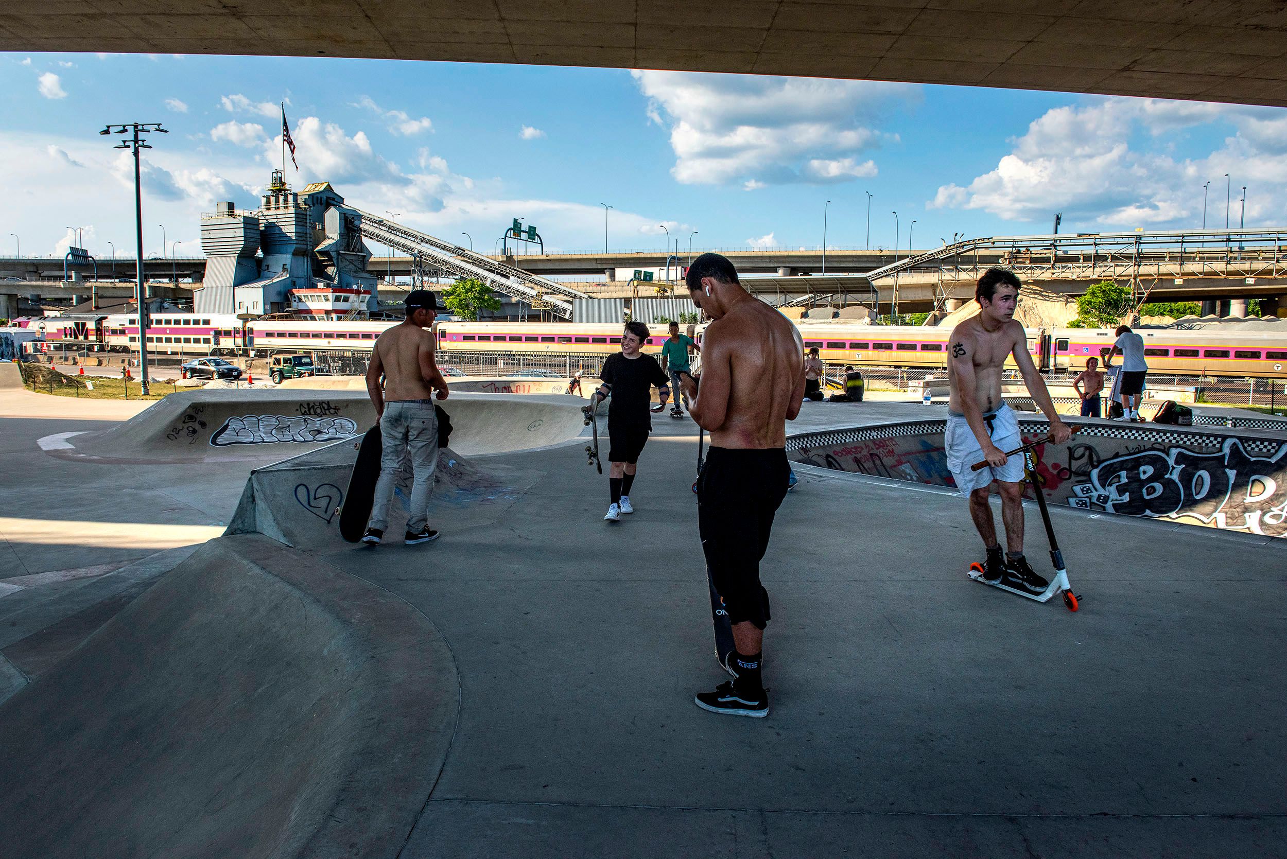 Photograph of people on scooters and skateboards hanging out and practicing moves on the different bowls and walls at the Lynch Family Skateboard Park in Cambridge, MA Lynch Family Skateboard Park
