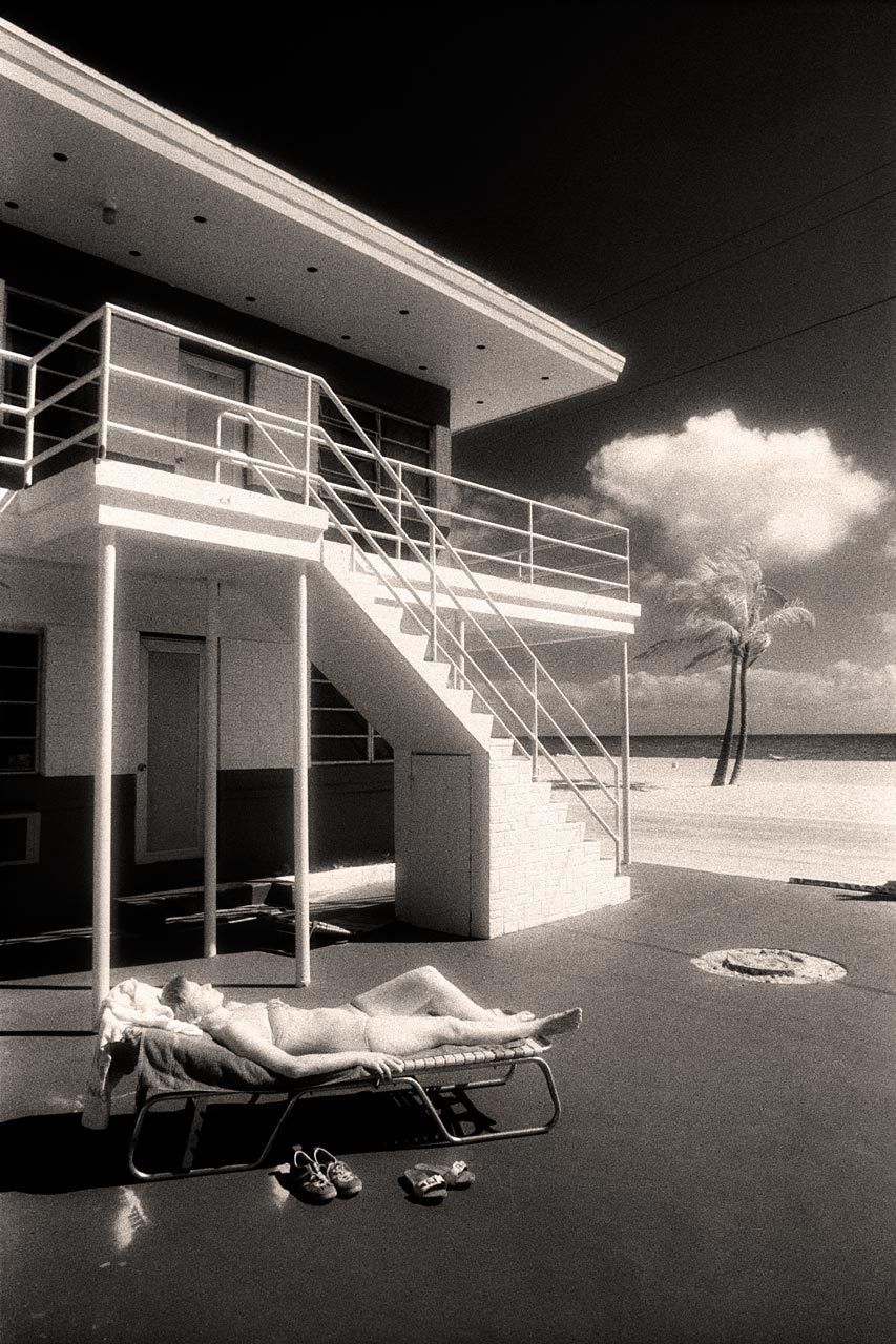 A sunbather soaks up rays by the boardwalk in Hollywood, Florida. Just north of the more famous beach in Miami, Hollywood is a polyglot enclave of European and French-Canadian tourists that's full of small, Art Deco-style motels and pensiones. This photograph's characteristic glow, as with the other infrared images, comes from the film's lack of an antihalation backing, an absence that allows light striking the emulsion's surface to spread out. 1sunbather_final
