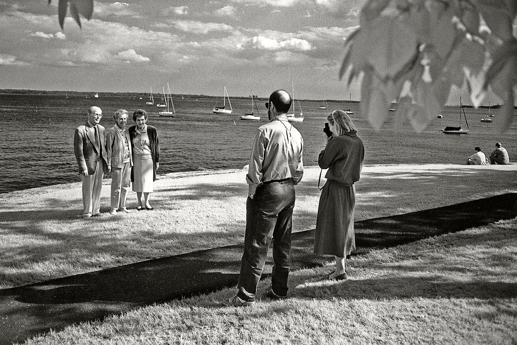 Casual observers of wedding photography pose in front of the Long Island Sound, at Manor Park in Larchmont, New York. 1trio
