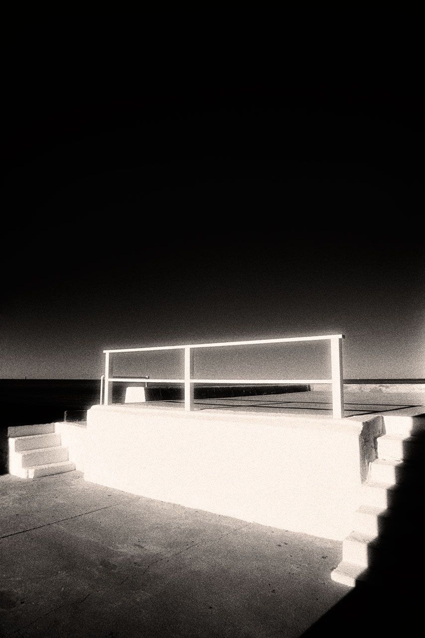 Photographed on Boston's South Shore, this concrete deck was built by the owners of the house across the street in order to enjoy their view of Massachusetts Bay. It was painted white, and the winter sun gave it a brilliance reminding me of Emerson's comment that "there is no object so foul that intense light will not make beautiful." Kodak infrared film's lack of the antihalation backing found in normal film caused the bright light to spread out when it struck the emulsion, creating a glowing effect. I aligned the middle horizontal element of the railing with the ocean horizon, a narrow black band at right. 1scituate_final