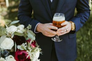 Groom holding drink with bouquet