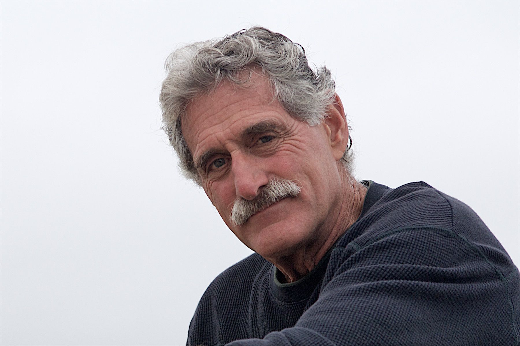 man in 60s. Older man with graying hair and a moustache looking into the camera man in 60s