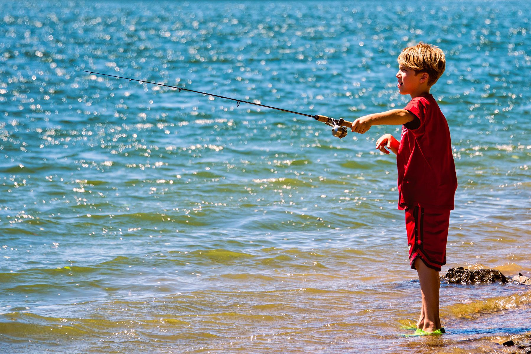 Little boy in red fishing with fishing rod
