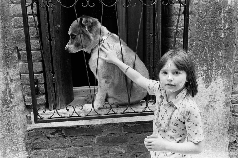 Girl with straps on face petting dog in window Vinicee Italy B&W street photography 1970 nineteen  seventies