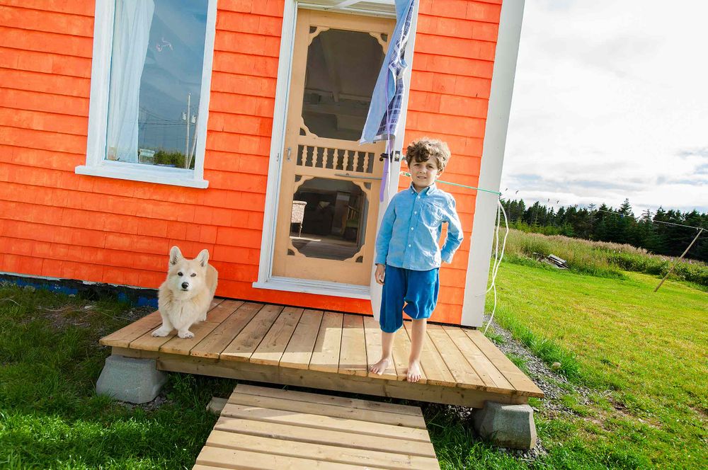 Boy on porch to orange house in Les Les Îles-de-la-Madeleine, Quebec Canada Orange
