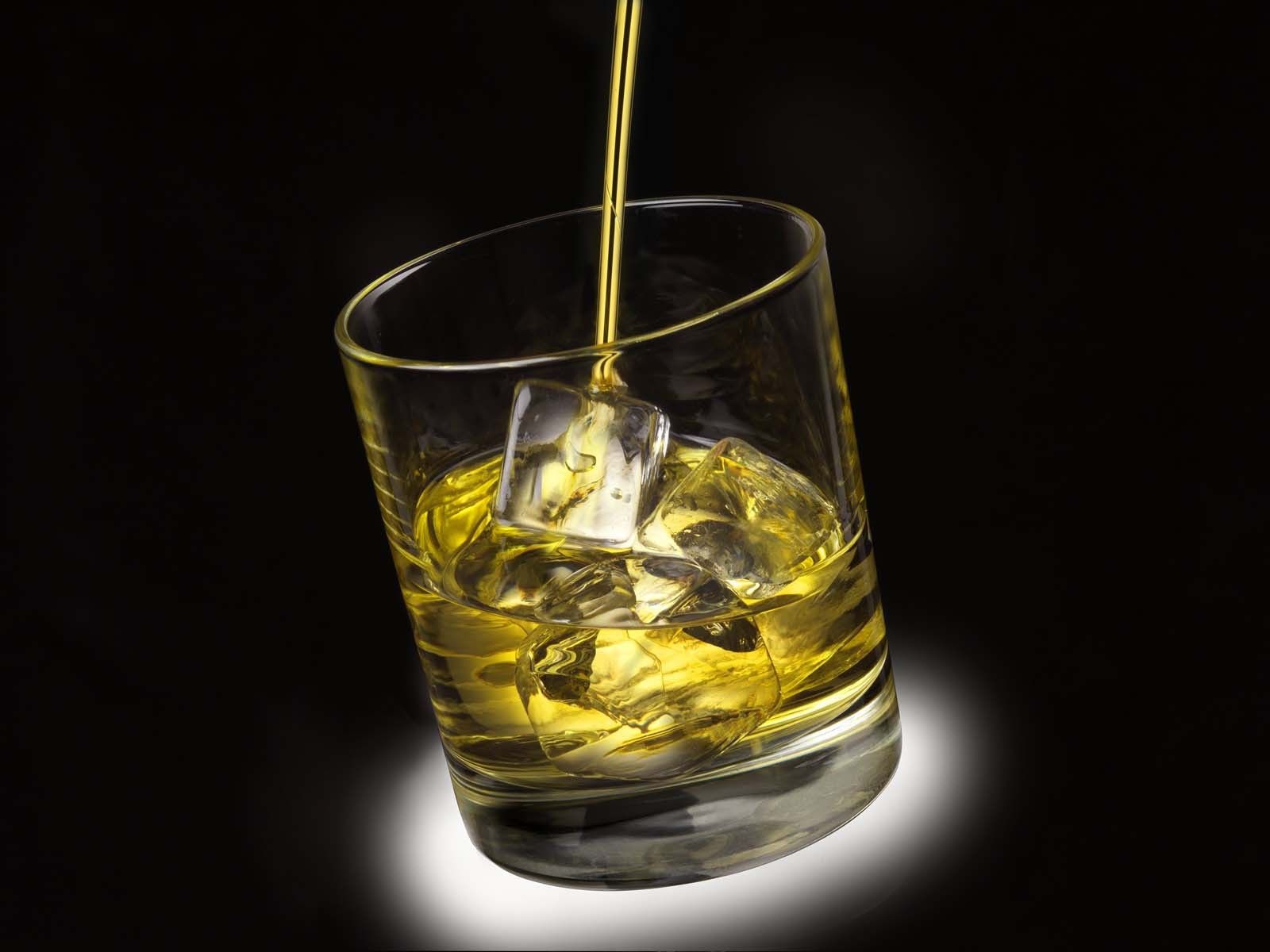 Glass of whisky with ice being poured.