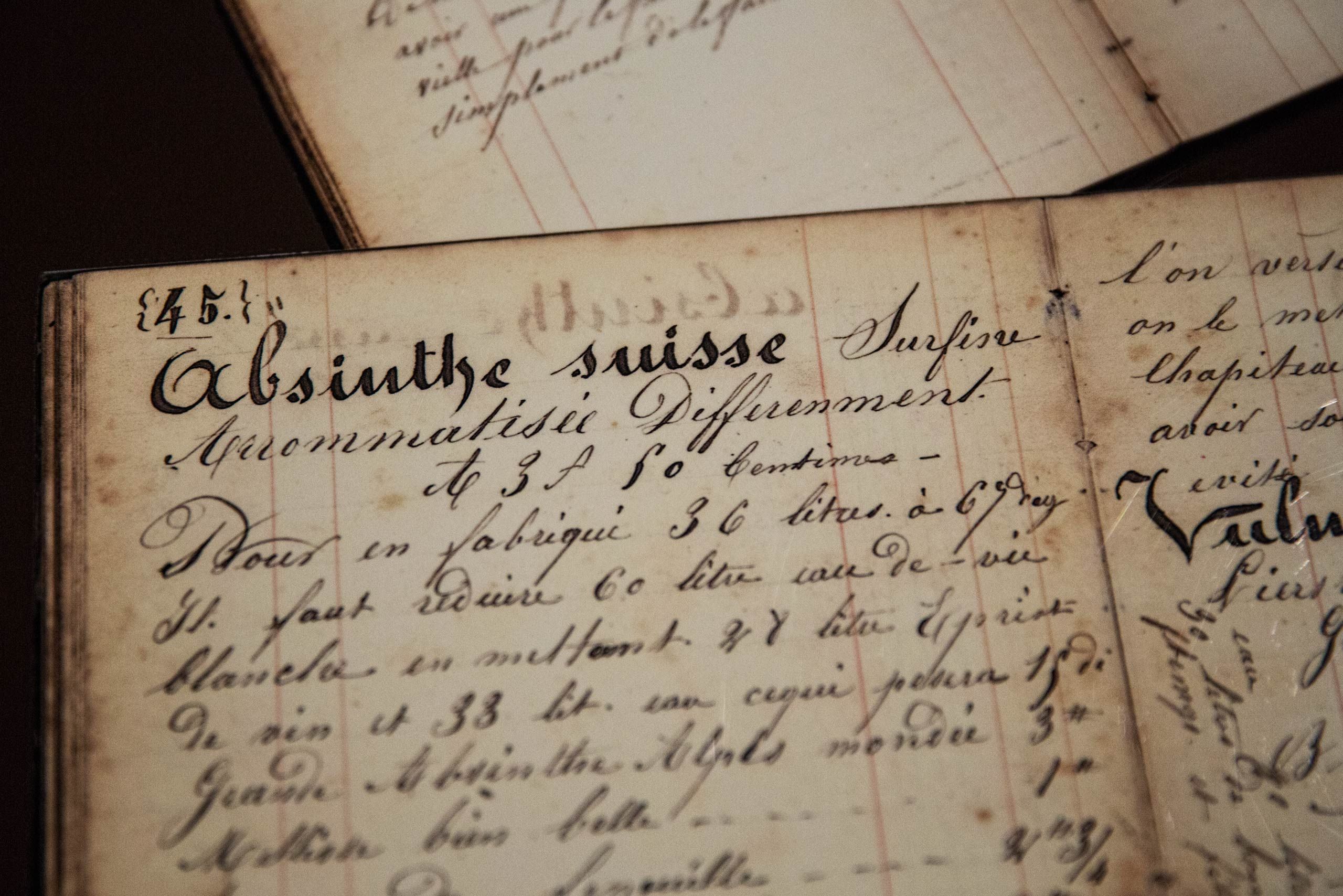 A photo of old absinthe family recipe written, in calligraphy, inside of an old journal. Photos of the mysterious spirit, absinthe, also called wormwood, green fairy, green muse located at Distillery Armand GUY in Pontarlier, France. This was a passion project and an amazing adventure into the world of absinthe, especially as on location photographer & location commercial photographer. Photo was shot with a shallow depth of field and selective focus. Old Absinthe Family Recipe