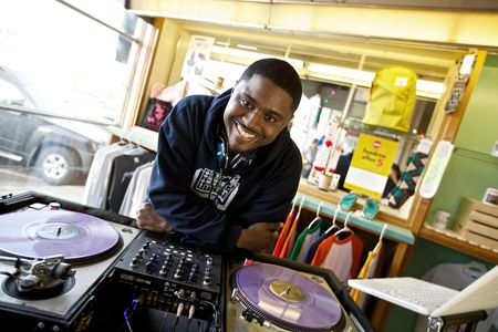 Portrait of a millennial DJ, leaning over vinyl records, with a big smile in Jackson, MS. Shot for the Mississippi Tourism campaign for advertising, branding, collateral and broadcast motion assets. Environmental portrait, and we are a industrial photographer, on location photographer & location commercial photographer. Shallow depth of field and selective focus. VisitMS DJ Smiling