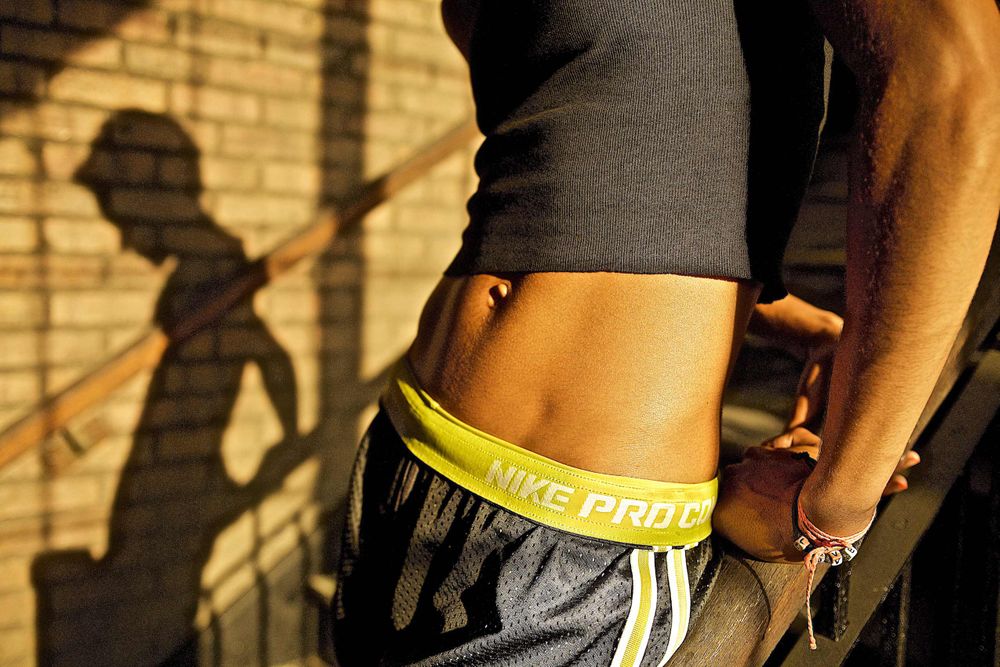 A photo of a woman's midriff with late afternoon light and shadows dressed in all Nike workout clothes in a gritty urban loft location. Midriff of Woman Wearing Nike Clothes