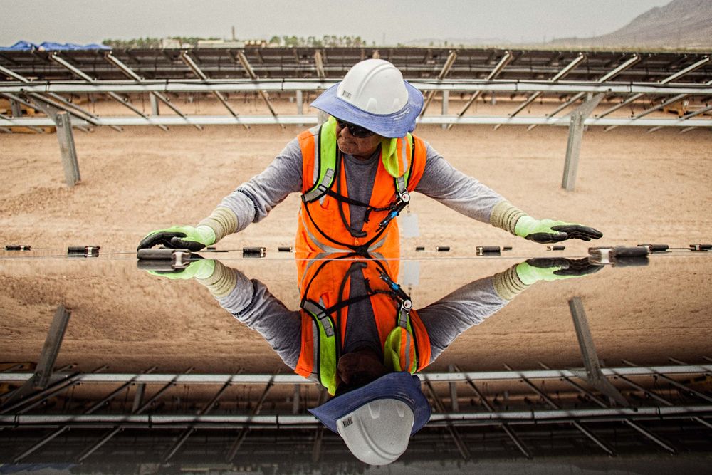 Environmental portrait of a worker installing a solar panel and highlighting the reflective quality of the panels. He is wearing protective glasses, helmet, vest etc. and wrapped and shielded from extreme heat, per OSHA requirement. This project was shooting a solar farm near El Centro, California, which is located right on the Mexico border. This energy collected from the sun will create free, off the grid, clean energy for many towns in California. As an industrial photographer, on location photographer & location commercial photographer this project was superb! Worker Installing a Solar Panel Showing His Reflection