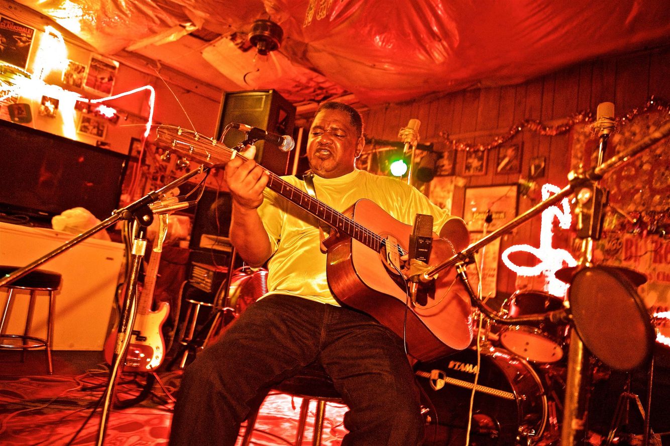 A photo of Louis "Gearshifter" Youngblood jamming on his guitar, performing at Red's Lounge Juke Joint in Clarksdale, Mississippi. Photos of various juke joints with people & locations on and around Highway 61, i the delta, and along the Blues Highway. These photographs were made for a number of projects such as the documentary We Juke Up In Here, the web series Moonshine & Mojo Hands and a passion project to document the beautiful Mississippi delta lifestyle. As an on location photographer, lifestyle photographer & location commercial photographer, this was one the best long term projects ever that captures southern Americana! Louis Gearshifter Youngblood at Red's Lounge Juke Joint