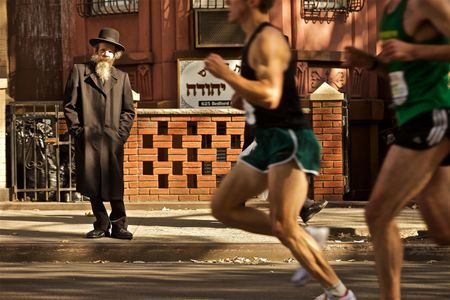 A Hasidic Jewish man is waiting to cross the street in Williamsburg Brooklyn NYC drink the NYC Marathon. NYC Marathon
