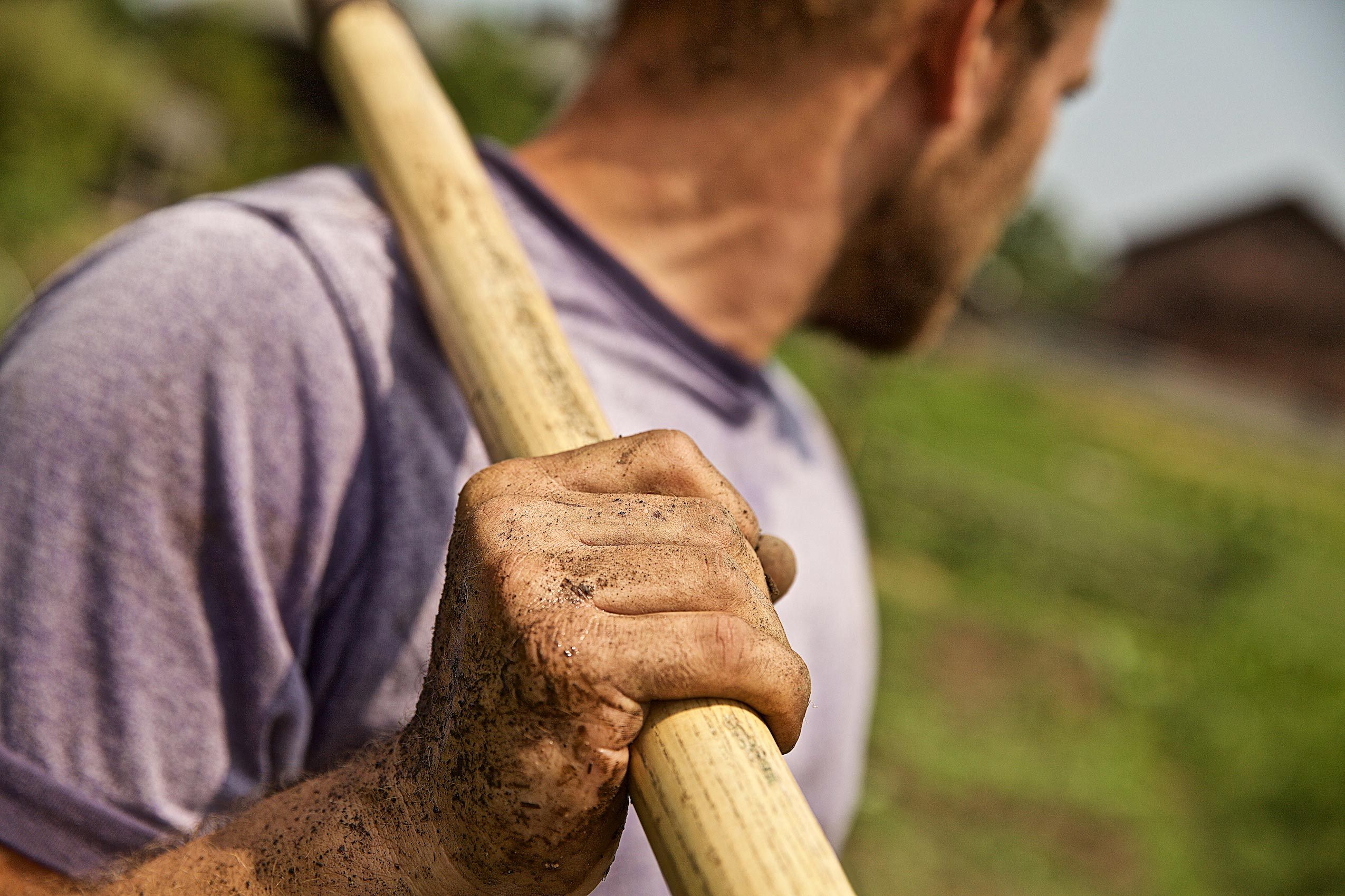 Male Farmer Looking at Farm Holding Hoe