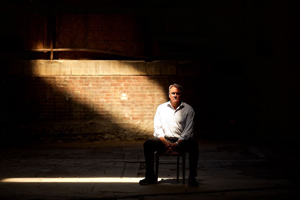 Environmental portrait of a man who lost his son to heroin. Photographed in an urban, vacant building in St. Louis with a streak of light and in part shadow. Selective focus. Photographed for a United Way advertising campaign. I am a advertising photographer, on location photographer & location commercial photographer. Photo of one of the many people that the United Way is assisting. Shallow depth of field. Dramatic Portrait of a Man In an Urban Environment