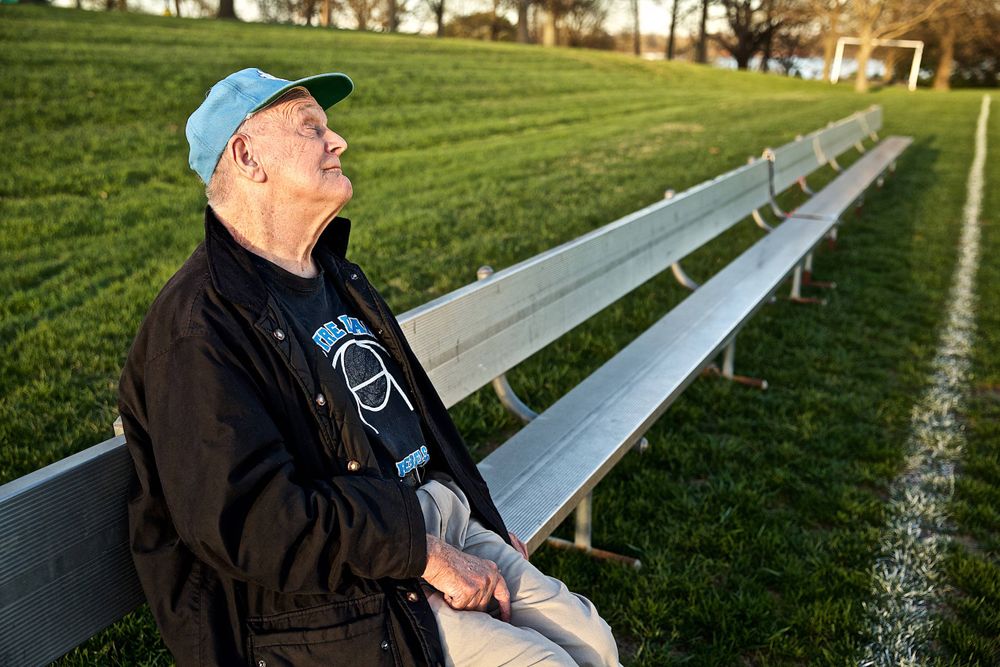 A blind man, senior citizen sitting a long bench at an athletic field in nice light and weather, very affectionate. Photographed for a United Way advertising campaign. I am a advertising photographer, on location photographer & location commercial photographer. Photo of one of the many people that the United Way is assisting. Blind Senior Citizen Sitting on a Bench