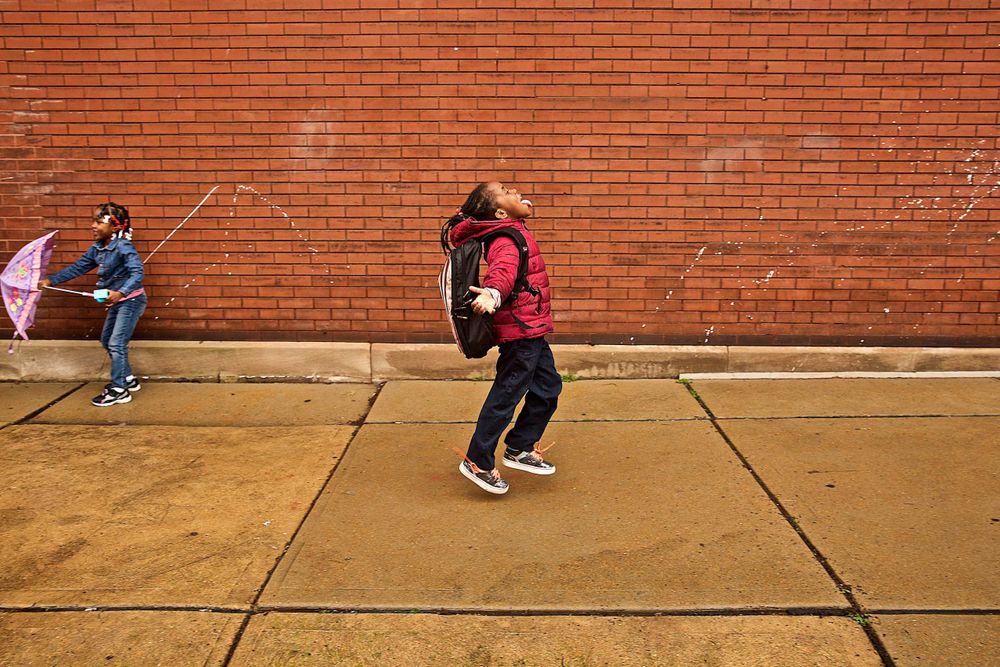 A photo of a young girl walking in the rain on an urban sidewalk, trying to catch rain drops in her mouth, having fun and smiling, very affectionate. Her sister is in the background. Photographed for a United Way advertising campaign. I am a advertising photographer, on location photographer & location commercial photographer. Photo of one of the many people that the United Way is assisting. Girl Catching Rain Drops With Her Mouth