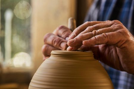Older male hands photographed tightly spinning a piece of pottery on a pottery wheel. The photo has motion blur.. Shot for the Mississippi Tourism campaign for advertising, branding, collateral and broadcast motion assets. Environmental portrait, and we are a industrial photographer, on location photographer & location commercial photographer. Shallow depth of field and selective focus. VisitMS Hands Making Pottery