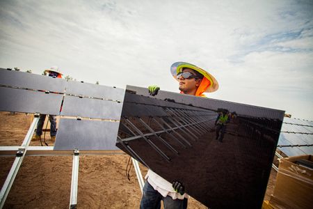 Environmental portrait of a worker holding and about to install a solar panel. The photo highlights the reflective quality of the panel. He is wearing protective glasses, helmet, vest etc. and wrapped and shielded from extreme heat, per OSHA requirement. This project was shooting a solar farm near El Centro, California, which is located right on the Mexico border. This energy collected from the sun will create free, off the grid, clean energy for many towns in California. As an industrial photographer, on location photographer & location commercial photographer this project was superb! Worker Holding a Solar Panel