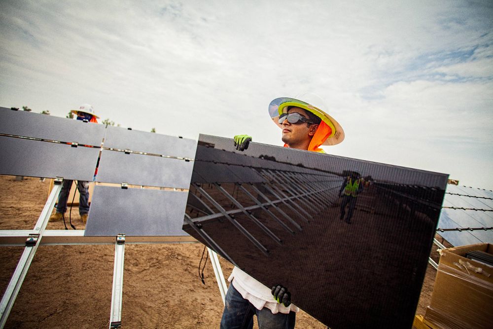 Environmental portrait of a worker holding and about to install a solar panel. The photo highlights the reflective quality of the panel. He is wearing protective glasses, helmet, vest etc. and wrapped and shielded from extreme heat, per OSHA requirement. This project was shooting a solar farm near El Centro, California, which is located right on the Mexico border. This energy collected from the sun will create free, off the grid, clean energy for many towns in California. As an industrial photographer, on location photographer & location commercial photographer this project was superb! Worker Holding a Solar Panel