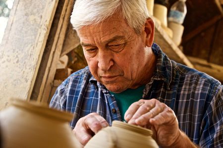 An older man, senior citizen intently works on a pottery wheel making a vase. Older Man Working on a Pottery Wheel