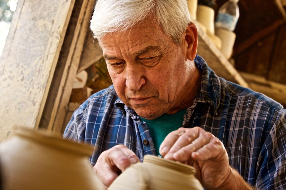 An older man, senior citizen intently works on a pottery wheel making a vase. Older Man Working on a Pottery Wheel