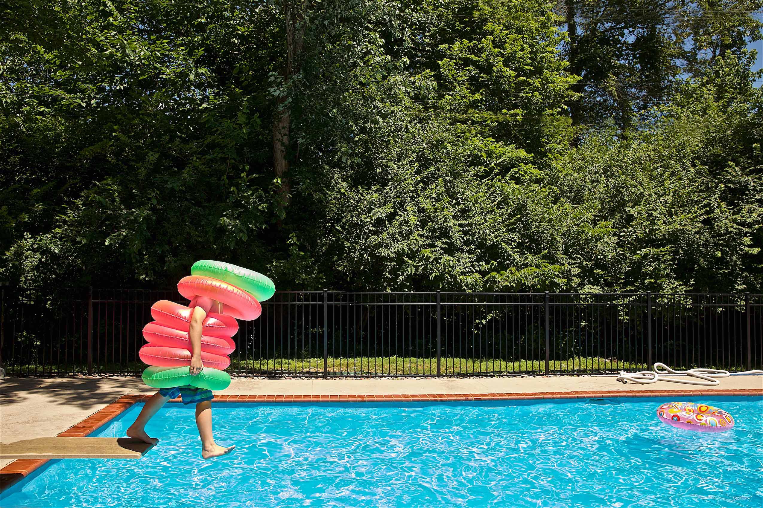 Boy Jumping off Diving Board with Many Pool Tubes