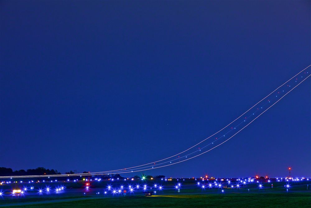 A wide photograph with a very slow shutter speed photograph of a cargo plane landing at an airport. The slow shutter speeds shows the exact trail the plane is on creating streaks through the night sky. Next stop, the other side of the world! This was a project shooting for the air cargo transportation industry. This project was amazing as an industrial photographer, on location photographer & location commercial photographer. Shallow depth of field and selective focus with slow shutter speed and some motion blur. Streaks of Airplanes in a Night Sky