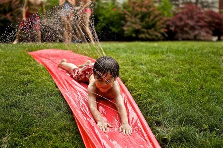 Young boy sliding down a water slide in a front yard. Boy on a Water Slide