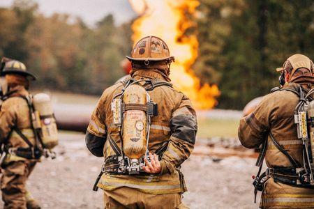 Photo of Loss Control people dressed in protective fire gear, facing a fire , explosion, training and ready for action and to respond and mitigate a disaster as it relates to risk management in the insurance industry. Environmental portrait, and we are a industrial photographer, on location photographer & location commercial photographer. Firemen Facing a Training Fire