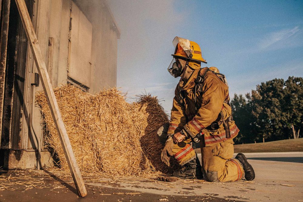 Photo of Loss Control person dressed in protective fire gear, training and ready for action and to respond and mitigate a disaster as it relates to risk management in the insurance industry. He is kneeling and preparing to enter a burin gin building. Environmental portrait, and we are a industrial photographer, on location photographer & location commercial photographer. Fireman Prepares to Enter a Burning Structure
