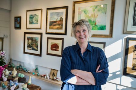 Portrait of a woman artist at her gallery. She smiling looking into the camera. Shot for the Mississippi Tourism campaign for advertising, branding, collateral and broadcast motion assets. Environmental portrait, and we are a industrial photographer, on location photographer & location commercial photographer. Shallow depth of field and selective focus. VisitMS Female Artist In a Gallery