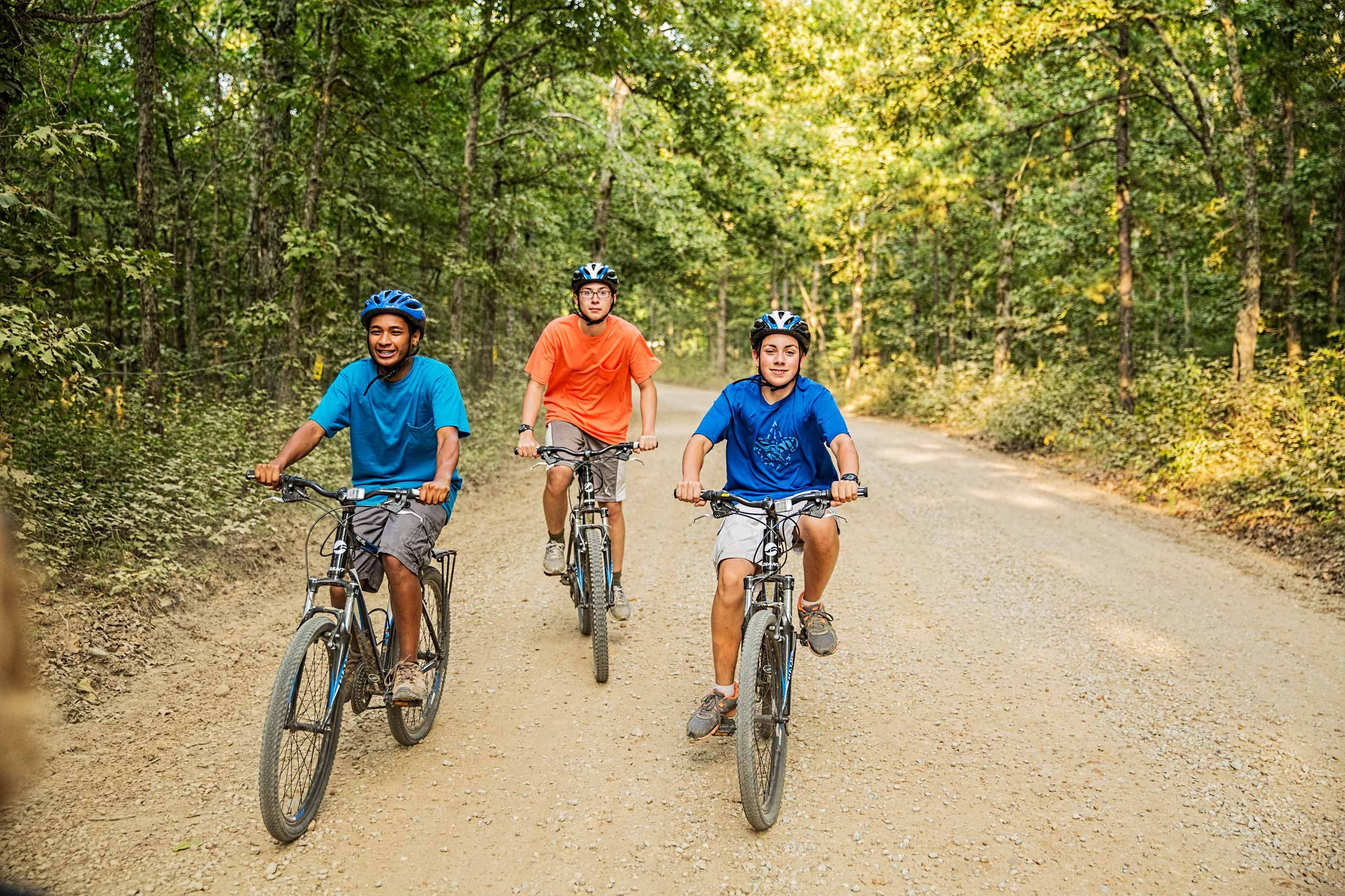 Three Boys Riding Bikes on a Dirt Road.