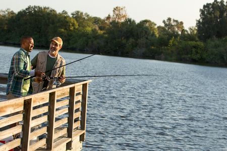 Friends fishing off of a lake dock smiling and having a good time at dawn. Men Fishing