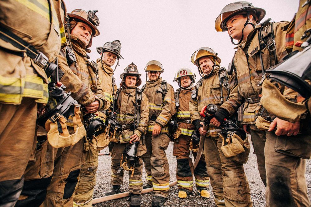A photo from a low angle of a group of firemen, loss control prevention specialists who are there to be trained with their instructors. Photo of Loss Control people dressed in protective fire gear, training and ready for action and to respond and mitigate a disaster as it relates to risk management in the insurance industry. Environmental portrait, and we are a industrial photographer, on location photographer & location commercial photographer. Group Photo of Loss Control Prevention Trainers and Trainees