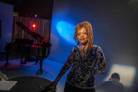 Portrait of notable jazz singer Cassandra Wilson on stage, smiling and looking into the camera, with dramatic lighting. Shot for the Mississippi Tourism campaign for advertising, branding, collateral and broadcast motion assets. Environmental portrait, and we are a industrial photographer, on location photographer & location commercial photographer. Shallow depth of field and selective focus. VisitMS Portrait of Cassandra Wilson