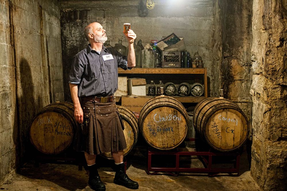 Photo at Schlafly Beer in St. Louis for an advertising campaign and image brand library. A brewmaster inspects a beer surrounded by casks or barrels of beer aging in a dimly lit room. Environmental portrait. As an industrial photographer, on location photographer & location commercial photographer this was a great project to be associated with. Shallow depth of field and selective focus. Brew Master Inspecting a Beer