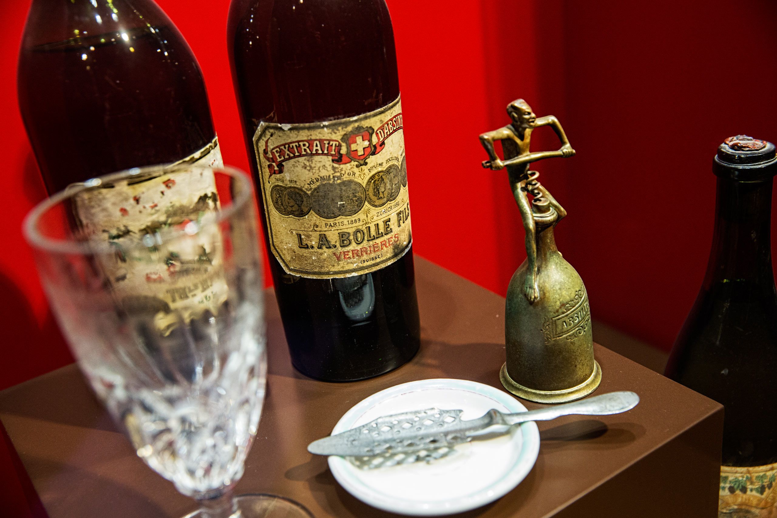 A photo of old absinthe bottles with peeling labels, an absinthe spoon and corkscrew. Photos of the mysterious spirit, absinthe, also called wormwood, green fairy, green muse located at Distillery Armand GUY in Pontarlier, France. This was a passion project and an amazing adventure into the world of absinthe, especially as on location photographer & location commercial photographer. Photo was shot with a shallow depth of field and selective focus. Old Absinthe Bottles, Labels and a Spoon