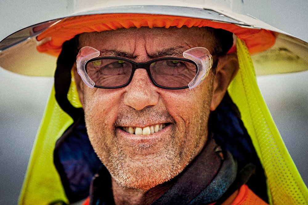 Environmental portrait of an older worker at the solar farm looking directly into the camera wearing protective glasses, helmet, vest etc. and wrapped and shielded from extreme heat. This project was shooting a solar farm near El Centro, California, which is located right on the Mexico border. This energy collected from the sun will create free, off the grid, clean energy for many towns in California. As an industrial photographer, on location photographer & location commercial photographer this project was superb! Shallow depth of field and selective focus Worker On a Solar Farm