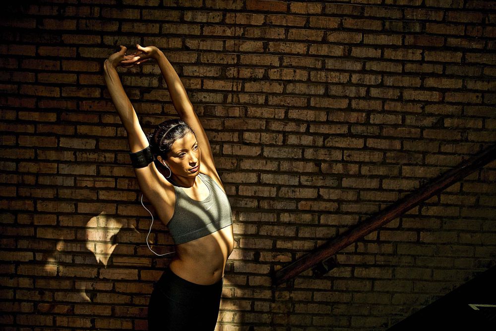 A photo of a woman stretching before a workout with late afternoon light and shadows dressed in all Nike workout clothes in a gritty urban loft location. Woman Stretches