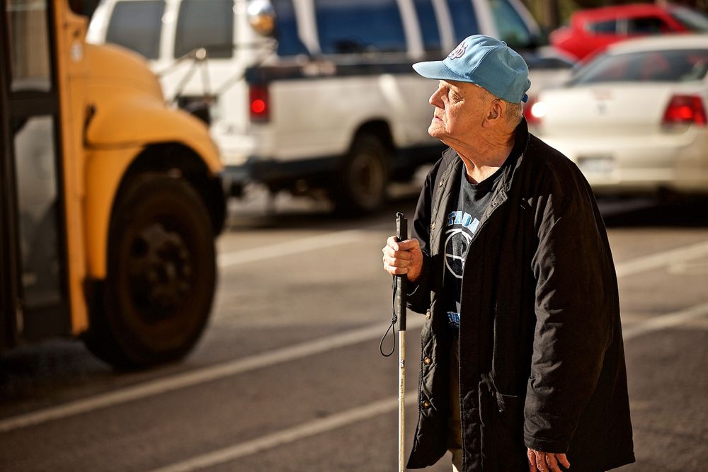 A photo of a senior citizen, blind man with a cane standing along a busy street facing lots of traffic . Photographed for a United Way advertising campaign. I am a advertising photographer, on location photographer & location commercial photographer. Photo of one of the many people that the United Way is helping out. Blind Senior Citizen Trying to Cross the Street