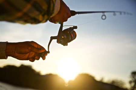 A early morning backlit , close up photo of a red fishing reel and hands as it's being cast. Close Up of Fishing Reel