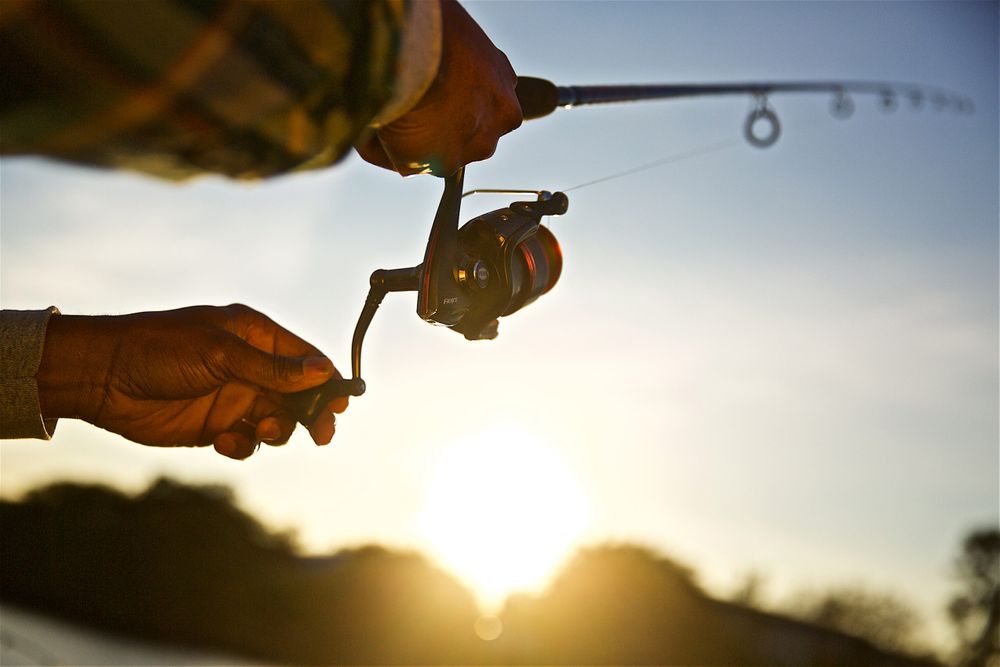 A early morning backlit , close up photo of a red fishing reel and hands as it's being cast. Close Up of Fishing Reel