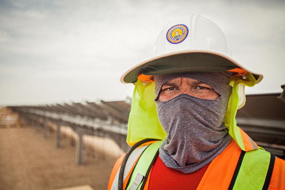 Environmental portrait of an older worker at the solar farm looking directly into the camera wearing protective helmet, vest etc. and wrapped and shielded from extreme heat. This project was shooting a solar farm near El Centro, California, which is located right on the Mexico border. This energy collected from the sun will create free, off the grid, clean energy for many towns in California. As an industrial photographer, on location photographer & location commercial photographer this project was superb! Worker Shielded From Heat
