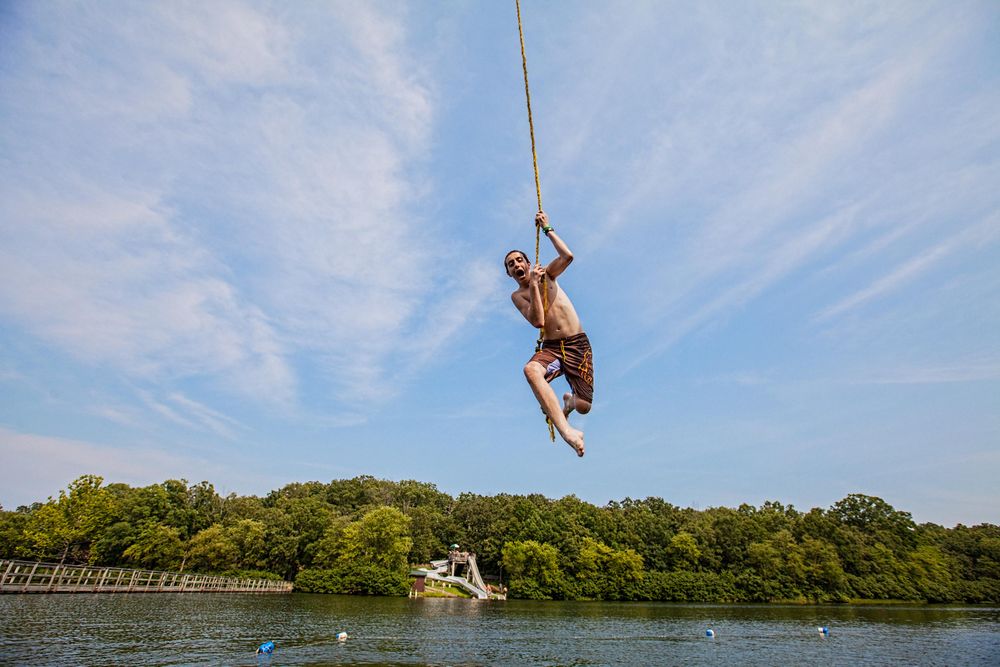 Photo of a boy swinging and jumping off a rope swing over a lake. Shoot commissioned by the Boy Scouts of America for their advertising and collateral campaign. Environmental portrait, advertising photographer, on location photographer & location commercial photographer. Boy On a Rope Swing Over a Lake
