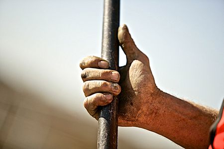 A close up photo of a workers dirty soiled hands holding a bar with shallow depth of field and selective focus. Workers Hand Holding a Bar